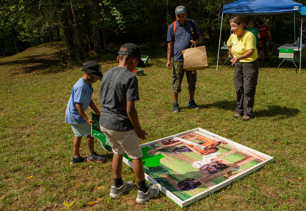 Two young boys places pieces of a large jigsaw puzzle on the grass as part of a Project Chimps program educating kids about chimps