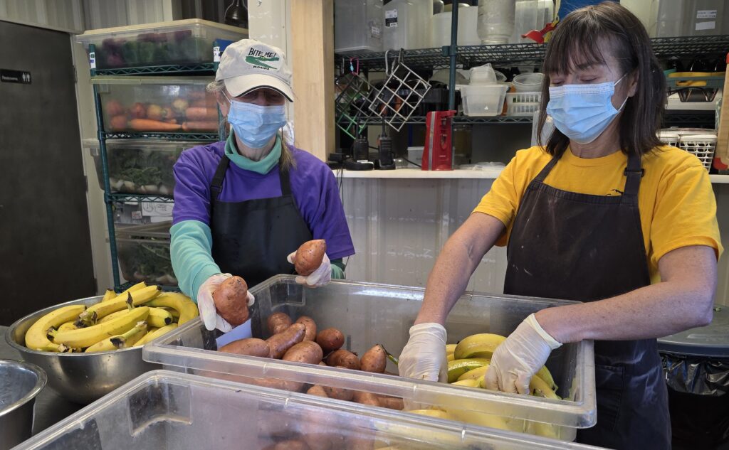 Volunteers Victoria and Luanne sort through potatoes and bananas in the kitchen.